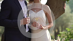 The bride and groom stand side by side and hold glasses of champagne in their hands