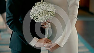 A bride and groom stand together and hold each other's hands.