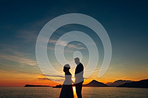 the bride and the groom standing on the on the beach of the Mamula island and holding hands at the sunset