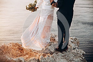 Bride and groom standing on cliff edge with sea beyond it