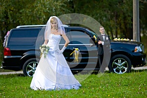 Bride and groom standing in front of wedding car