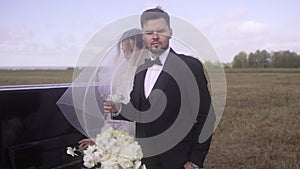 a bride and groom are standing next to a limousine in a field