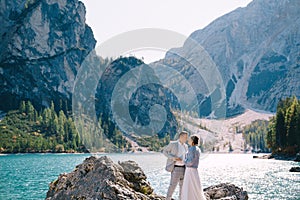 The bride and groom are standing on stones overlooking the Lago di Braies in Italy. Destination wedding in Europe, on