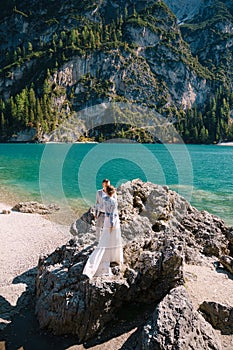 The bride and groom are standing on stones overlooking the Lago di Braies in Italy. Destination wedding in Europe, on