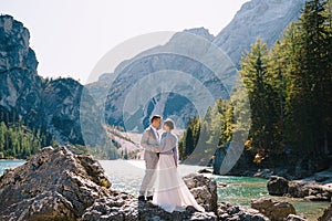 The bride and groom are standing on stones overlooking the Lago di Braies in Italy. Destination wedding in Europe, on