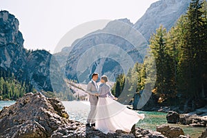 The bride and groom are standing on stones overlooking the Lago di Braies in Italy. Destination wedding in Europe, on