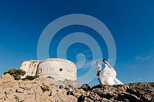 Bride and groom are standing together and holding hands near the Arza fortress on the Mamula island