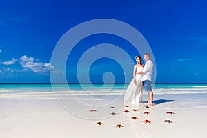 Bride and Groom standing on tropical beach shore with red starfish in the sand