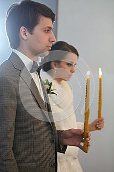 Bride and groom standing at wedding ceremony. Happy stylish wedding couple holding candles with light under golden