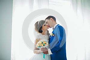 Bride and groom in studio light stand kiss on a white background