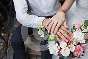 A bride and groom with their hands on top of the flowers, showing off their rings