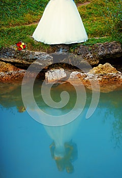 Bride and groom together in landscape by a lake reflected on water surface - romantic wedding concept.