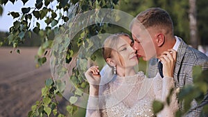 Bride and groom touching and enjoying each other against a backdrop of birch tree branches.