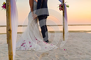 The bride and groom under archway on beach. Calm and romantic white sandy beach for honeymoon destination and love background