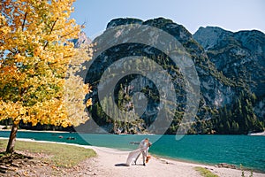 Bride and groom under an autumn tree, with fiery yellow foliage, at the Lago di Braies in Italy. Destination wedding in