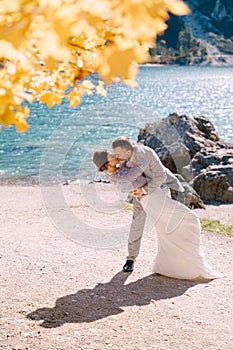 Bride and groom under an autumn tree, with fiery yellow foliage, at the Lago di Braies in Italy. Destination wedding in