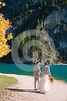 Bride and groom under an autumn tree, with fiery yellow foliage, at the Lago di Braies in Italy. Destination wedding in