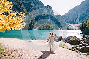 Bride and groom under an autumn tree, with fiery yellow foliage, at the Lago di Braies in Italy. Destination wedding in