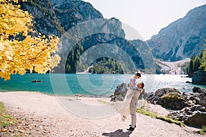 Bride and groom under an autumn tree, with fiery yellow foliage, at the Lago di Braies in Italy. Destination wedding in