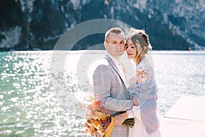 The bride and groom walk along a wooden boat dock at the Lago di Braies in Italy. Wedding in Europe, on Braies lake