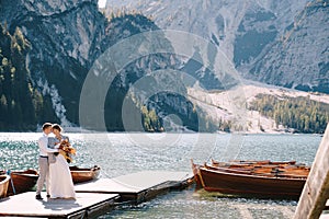 The bride and groom walk along a wooden boat dock at the Lago di Braies in Italy. Wedding in Europe, on Braies lake