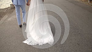 The bride and groom walk side by side holding hands, back view