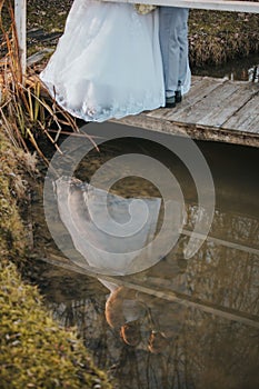 Bride and groom walk on a wooden platform over a pond