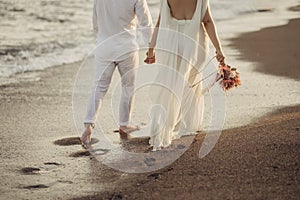 Bride groom walking on choppy Beach, bride has flowers in her hand