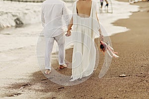 Bride groom walking on choppy Beach, bride has flowers in her hand