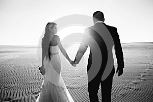 The bride and groom are walking in the desert, black and white photo, sunset