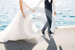 The bride and groom are walking hand in hand on the road by the sea, close-up