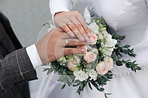 Bride and groom wearing beautiful engagement rings with bouquet outdoors, closeup