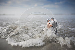 Bride and Groom Wedding Cake Topper Wearing Surgical Masks in the Waves of the Ocean