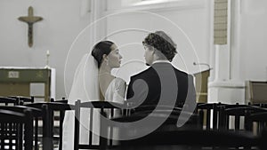 Bride and groom at the wedding ceremony in modern church. Action. Woman and man sitting together among empty seats.