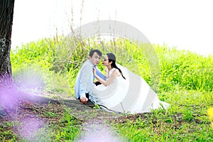 Bride and groom in wedding dress with elegant hairstyle, with white wedding dress Sitting in the grass by the river