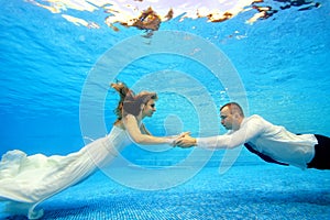 The bride and groom in wedding dresses swim underwater in the pool to meet each other. Portrait