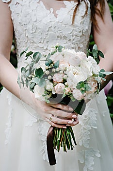 The bride holding a beautiful wedding bouquet of pastel, pink, peonies, roses flowers, greenery.