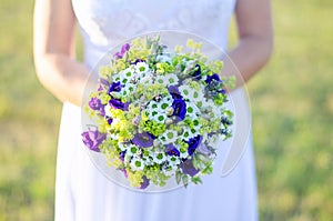 Bride holding a bouquet of flowers in a rustic style on meadow. Wedding bouquet.