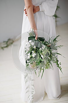 Bride holding a bouquet of lush green foliage and white flowers in her elegant wedding dress