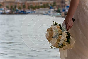 Bride Holding Bride`s Bouquet in front of the Sea on Blurred Taranto Vecchia Bluildings Background in Italy. Abandoned Bride. Wif