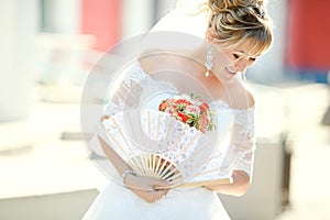 Bride holding fan and wedding bouquet, outdoors