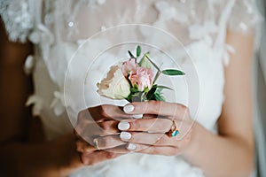The bride holding in hand close-up the groom buttonhole flowers with white roses, and green and greenery. Bride`s Preparations