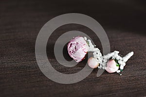 The bride holding in hand close-up the groom`s buttonhole flowers with white roses, and green and greenery