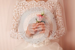 The bride holding in hand close-up the groom`s buttonhole flowers with white roses, and green and greenery