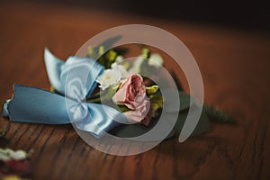 The bride holding in hand close-up the groom`s buttonhole flowers with white roses, and green and greenery