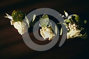 The bride holding in hand close-up the groom`s buttonhole flowers with white roses, and green and greenery