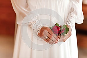 The bride holding in hand close-up the groom`s buttonhole flowers with white roses, and green and greenery