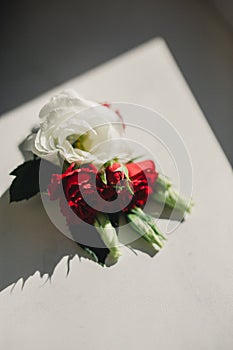 The bride holding in hand close-up the groom`s buttonhole flowers with white roses, and green and greenery