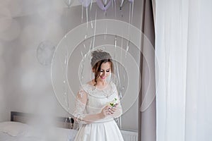 The bride holding in hand close-up the groom`s buttonhole flowers with white roses, and green and greenery. Bride`s Preparations