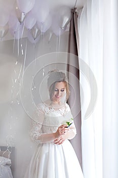 The bride holding in hand close-up the groom`s buttonhole flowers with white roses, and green and greenery. Bride`s Preparations